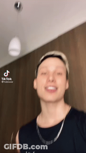 A Man Wearing A Black Shirt And A Silver Chain Is Smiling . GIF