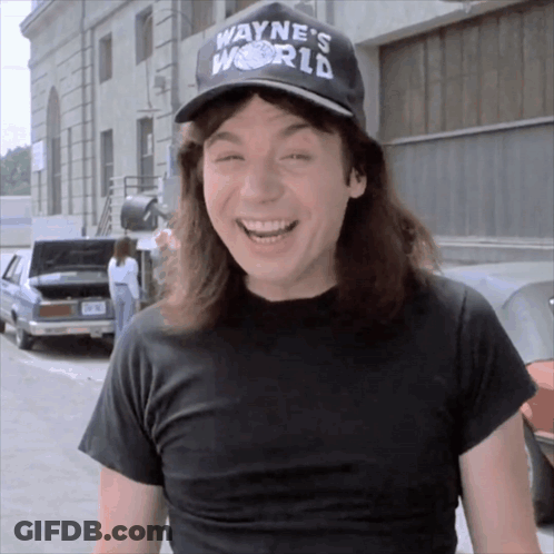 A Man Wearing A Black Shirt And A Wayne 'S World Hat Smiles GIF