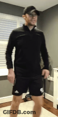 A Man Wearing A Black Shirt And Black Shorts Is Standing In A Room GIF