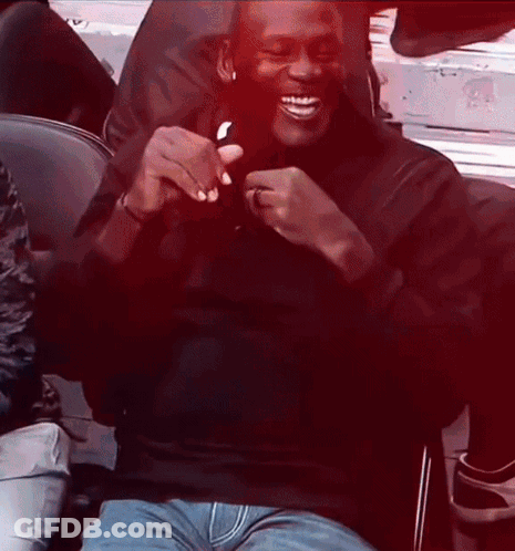 A Man Wearing A Black Shirt And Blue Jeans Is Sitting In A Chair And Smiling GIF