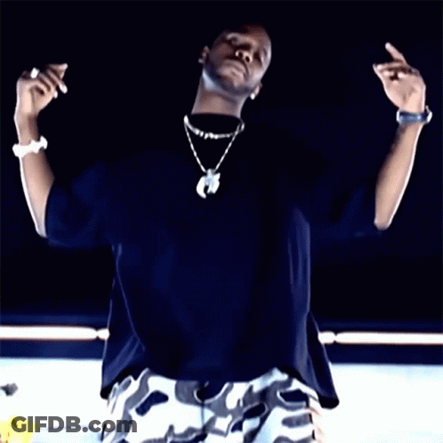 A Man Wearing A Black Shirt And White Camo Shorts Is Making A Peace Sign GIF