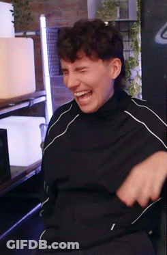 A Man Wearing A Black Shirt Is Laughing With His Mouth Open GIF
