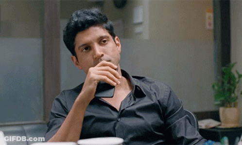 A Man Wearing A Black Shirt Is Sitting At A Table With His Hand On His Chin GIF