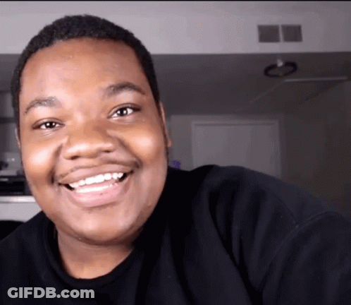 A Man Wearing A Black Shirt Is Smiling And Looking At The Camera GIF