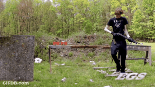A Man Wearing A Black Shirt That Says A Eagle Holds A Gun GIF