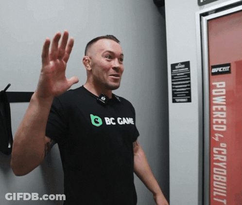 A Man Wearing A Black Shirt That Says Bc Game Waves His Hand GIF