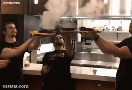 A Man Wearing A Black Shirt That Says Cava On It Holds Up A Tray Of Food GIF