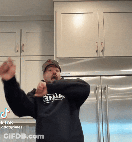 A Man Wearing A Black Shirt That Says Civil Is Standing In Front Of A Refrigerator GIF