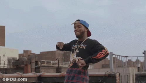 A Man Wearing A Black Shirt That Says " Die " Is Standing On A Rooftop . GIF