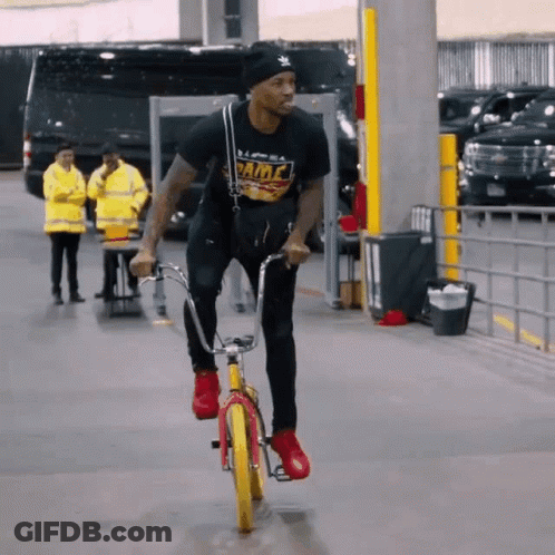 A Man Wearing A Black Shirt That Says Fame Is Riding A Bicycle GIF