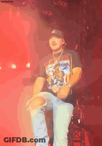 A Man Wearing A Black Shirt That Says Iron Maiden Is Dancing On A Stage GIF