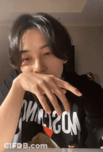 A Man Wearing A Black Shirt That Says Moschino Covering His Mouth With His Hand GIF