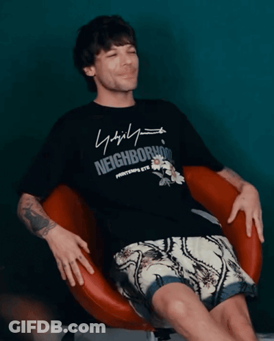 A Man Wearing A Black Shirt That Says Neighborhood Sits In A Chair GIF