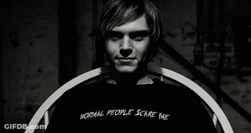 A Man Wearing A Black Shirt That Says `` Normal People Scare Me '' Is Sitting In A Chair . GIF