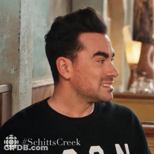 A Man Wearing A Black Shirt That Says Schitts Creek On It GIF