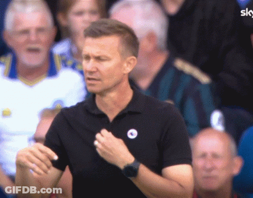 A Man Wearing A Black Shirt With A Blue Circle On It Stands In Front Of A Crowd GIF