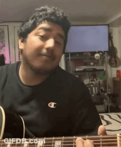 A Man Wearing A Black Shirt With A Champion Logo On It Playing A Guitar GIF