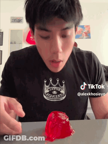 A Man Wearing A Black Shirt With A Crown On It Looks At A Red Jelly GIF