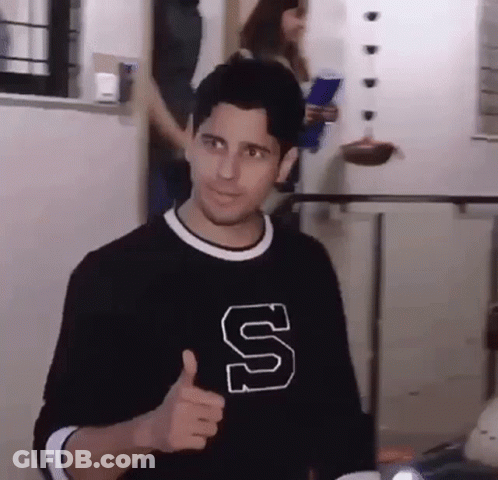 A Man Wearing A Black Shirt With A Letter S On It Is Giving A Thumbs Up . GIF