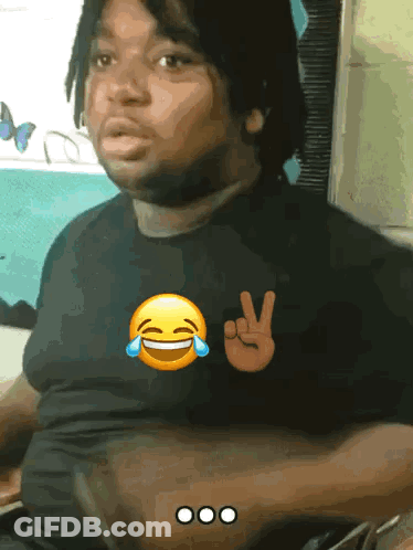 A Man Wearing A Black Shirt With A Peace Sign And A Laughing Face GIF