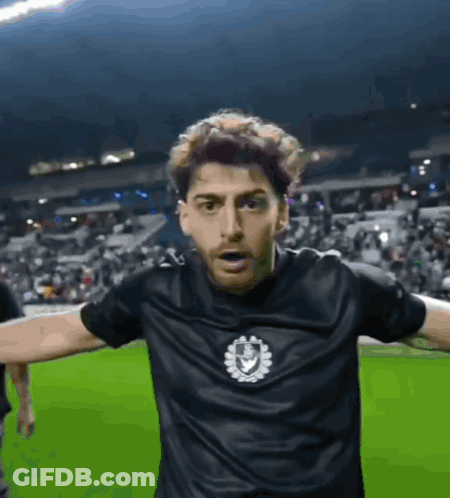 A Man Wearing A Black Shirt With A Shield On It GIF