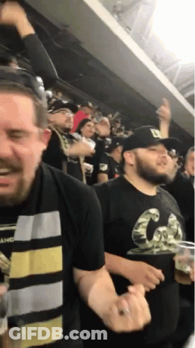 A Man Wearing A Black Shirt With The Letter D On It Stands In A Crowd GIF