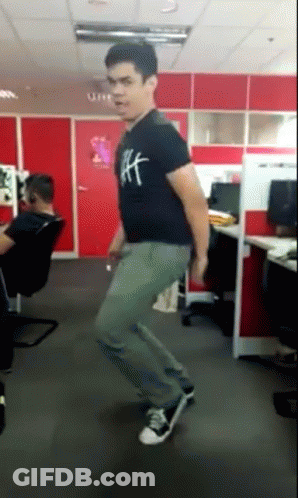 A Man Wearing A Black Shirt With The Letter H On It Is Dancing In An Office GIF