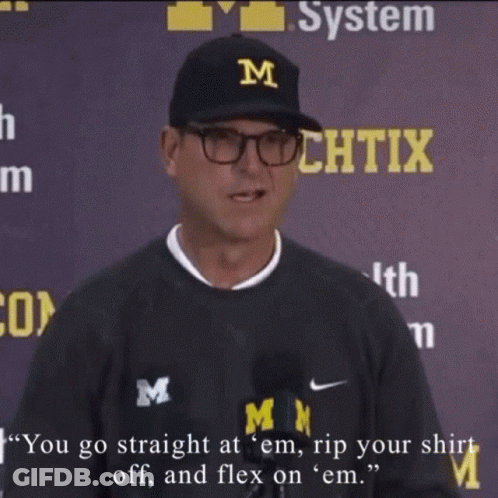 A Man Wearing A Black Shirt With The Letter M On It Is Talking Into A Microphone GIF
