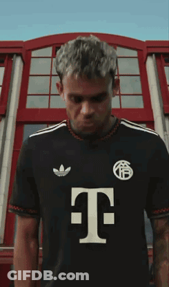 A Man Wearing A Black Shirt With The Letter T On The Front GIF