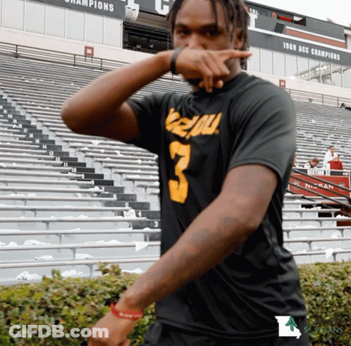 A Man Wearing A Black Shirt With The Number 3 On It Stands In Front Of A Stadium GIF
