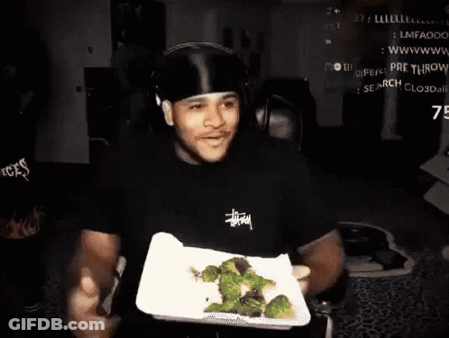 A Man Wearing A Black Stussy Shirt Is Holding A Plate Of Broccoli In His Hands GIF