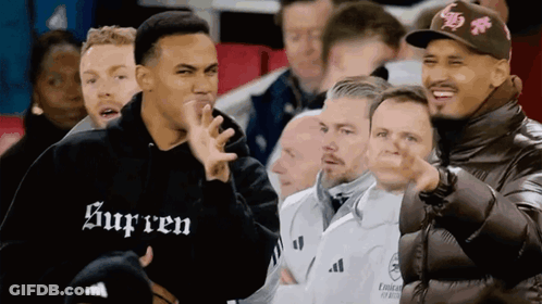 A Man Wearing A Black Supreme Sweatshirt Stands In A Crowd Of People GIF
