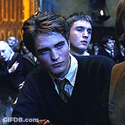A Man Wearing A Black Sweater And Tie Looks At The Camera GIF