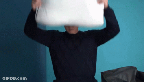 A Man Wearing A Black Sweater Is Holding A White Pillow Over His Head . GIF