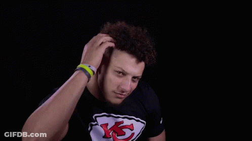 A Man Wearing A Black T-Shirt With A Chiefs Logo On It Is Holding His Hair . GIF