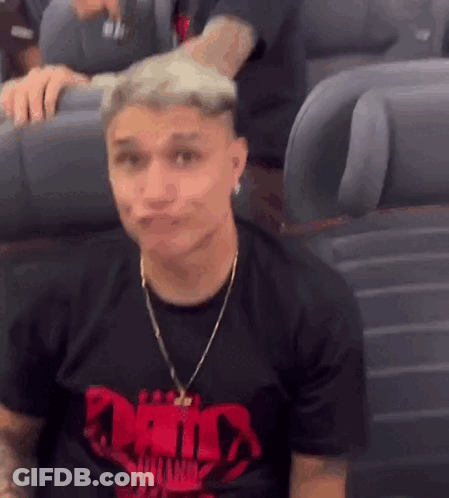 A Man Wearing A Black T-Shirt With A Red Skull On It Is Sitting On A Plane Making A Face . GIF
