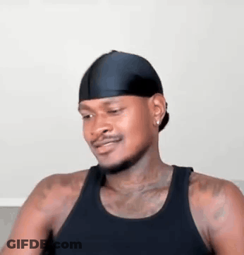 A Man Wearing A Black Tank Top And A Black Headband Is Sitting On A Couch . GIF