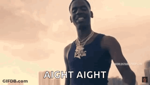A Man Wearing A Black Tank Top And A Necklace Is Standing In Front Of A Sunset . GIF