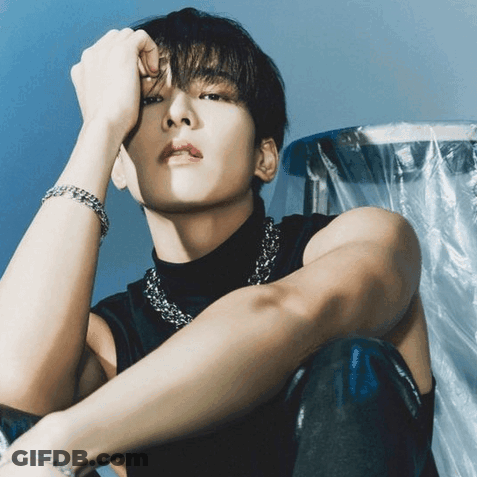 A Man Wearing A Black Tank Top And A Silver Chain Around His Neck Is Sitting Down GIF