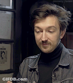 A Man Wearing A Black Turtleneck And A Denim Jacket Is Looking At Something GIF
