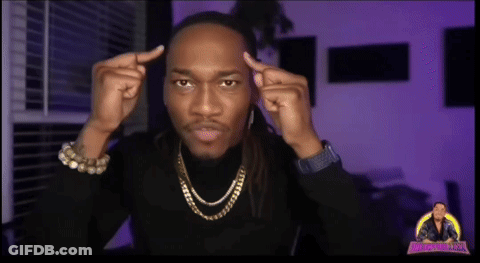 A Man Wearing A Black Turtleneck And Gold Chains Looks At The Camera GIF
