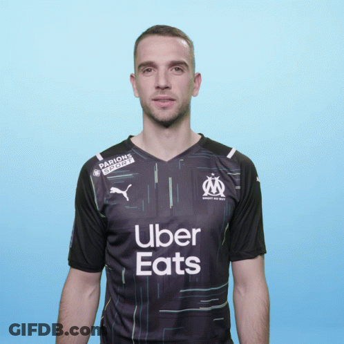 A Man Wearing A Black Uber Eats Shirt Stands In Front Of A Blue Background GIF
