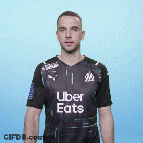 A Man Wearing A Black Uber Eats Shirt Stands In Front Of A Blue Background GIF