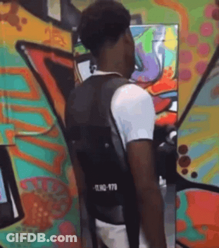 A Man Wearing A Black Vest Is Standing In Front Of A Colorful Graffiti Wall . GIF