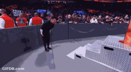 A Man Wearing A Black Wrestler 'S Hat Stands On A Stage GIF