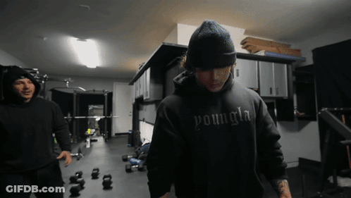 A Man Wearing A Black Youngla Hoodie Stands In A Gym GIF