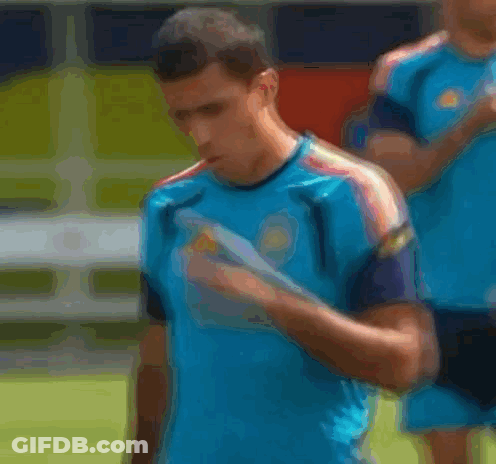 A Man Wearing A Blue Adidas Shirt Is Covering His Mouth With His Hand . GIF