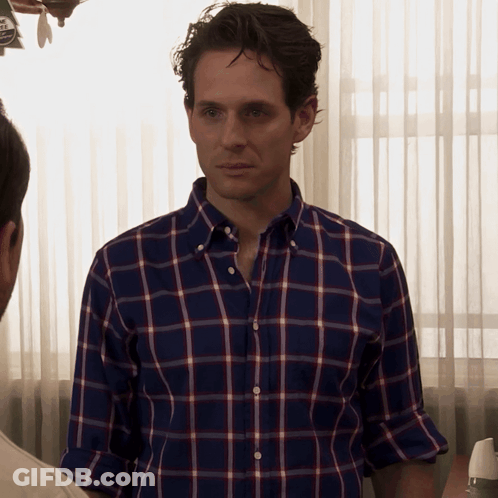 A Man Wearing A Blue And Red Plaid Shirt Is Standing In Front Of A Window GIF