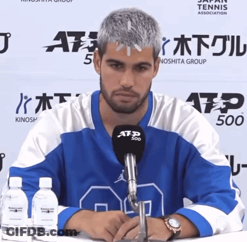 A Man Wearing A Blue And White Atp 500 Jersey Sits At A Table GIF