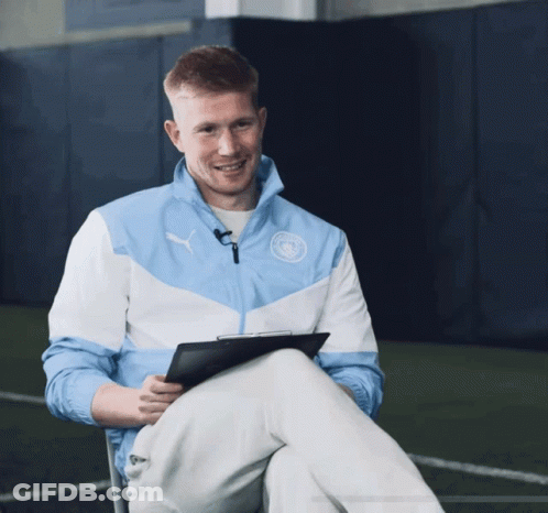 A Man Wearing A Blue And White Puma Jacket Sits With His Legs Crossed GIF